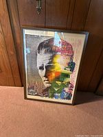 Full front view of the framed multi-colored Arcade Fire concert poster with a grayscale portrait, in a silver IKEA frame.