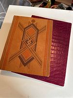 Two leather notebooks - one brown with geometric design, one red embossed crocodile pattern - stacked on a white surface