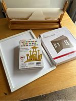 Ikea wooden paper roll holder with torn white paper roll, wooden blocks box on white tray, and Ashland miniature room kit box on wooden table.