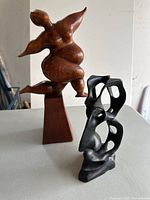 Two sculptures: wooden dancing woman and black stone abstract face side by side on surface.
