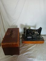 Singer antique sewing machine on wooden base next to carrying case.