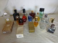 Group photo of 15 assorted perfume and cologne bottles on a beige cloth background, various brands and styles visible including boxed items.