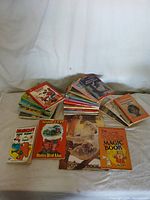 Wide view of multiple stacks of children's hard bound books showing various cover designs and titles including Heathcliff and Adam & Eve.