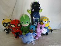 Frontal view of 9 assorted plush toys sitting on a beige surface, showing detailed characters including Spider-Man, Minion, and others.