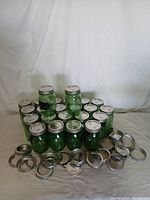 Full lot of 24 green Ball Mason jars with silver lids shown arranged in a pyramid. Some lids are loose and placed in front.