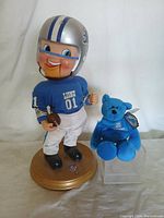 Front view of Detroit Lions singing figure and blue Beanie Baby bear against white background.
