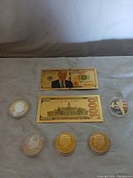 Full view of all coins and novelty bills featuring Donald Trump and a St. Michael medallion on cloth surface.