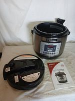 Nu-Wave Nutri-Pot 6 Qt Digital Pressure Cooker with lid and owner's manual laid out on beige surface with white backdrop.