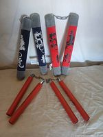 Full view of the two pairs of practice nunchucks; plush padded set in red and navy blue with dragon designs at the back, and red wooden traditional nunchucks in front.