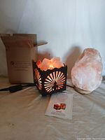 Two salt rock lamps shown: one illuminated in decorative metal basket with sunburst sides, the other a standalone salt lamp on wooden base with plug and instructions visible