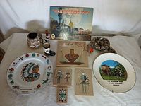 Photo of western-themed collectibles including plates, pottery, wooden art, and a ceramic boot arranged on a white surface.