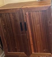 Closed view of wood wine cabinet showing natural wood finish and black handles on two doors.