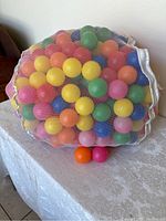 Over 100 brightly colored hollow plastic balls inside a white mesh bag, sitting on a table. Balls include yellow, green, orange, pink, blue and purple.