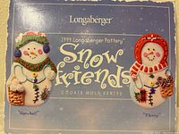 Photo of the front of the box showing two colorful ceramic snowman cookie molds named Snowball and Flurry from the 1999 Longaberger Snow Friends series.