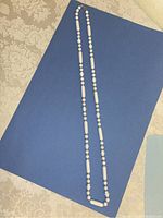 Full length photo of the white bead necklace showing white round and elongated beads against a blue background