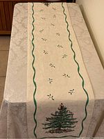 Full length view of cream damask table runner laid on table showing leaf motifs, green wavy border, and Christmas tree embroidery near one end