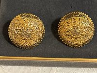 Front view of Luisa Conti oval clip-on earrings showing intricate raised gold-tone design.