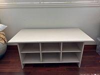 Full front view of the off-white solid wood table showing six cubbies and the table's overall shape and structure.