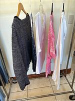 Five Free People tops hanging on rack: dark grey knit sweater, three white tops varying in sleeve length and style, pink tie-dye short sleeve top