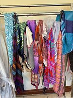 Various women's scarves hanging from a rack showing colors, patterns, and fabric types.