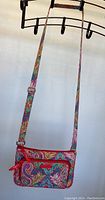 Full view of colorful Vera Bradley crossbody purse hanging on rack showing overall design and strap.