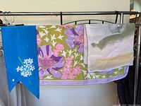 Three Vera Neumann scarves hanging on a rack showing various colors and patterns.