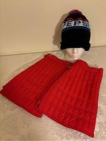 Red quilted gaiters and black Pepsi winter hat set displayed on a mannequin head and tabletop.
