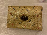 Front view of light gold fabric clutch purse with multicolor leaf pattern and gold-tone turn-lock clasp.