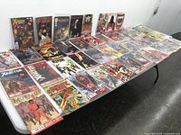 Wide view of assorted comic books laid out on a table, featuring multiple titles and vibrant covers in plastic sleeves.