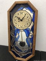 Full front view of the custom octagonal wall clock showing wood frame, decorative stained and mirrored glass, pendulum, and clock face.