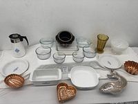 Full lot on white surface showing all dishes, glass bowls, copper molds, and Corning Ware coffee pot