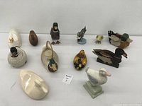 Overview photo showing 11 assorted duck figurines in various materials including ceramic and wood, ranging from realistic mallards to stylized figures.