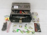Fishing tackle box open showing multiple trays with assorted fishing gear including bobbers, lures, hooks, lines, and small containers.