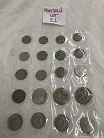 View of 18 assorted foreign coins in plastic coin sleeves arranged in rows on white fabric background, showing various designs and sizes.