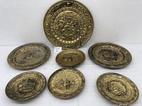 Overview of the set of six gold metallic embossed wall plates with various detailed scenes and ornate borders.