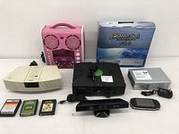 Overview of all miscellaneous electronics including Bose Wave Radio, pink karaoke machine, Xbox Kinect, Xbox 360 console, boxed PowerSat, game cartridges, USB flash drive, and handheld gaming device.