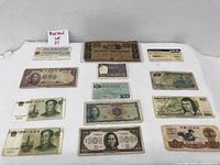 Multiple international paper currency notes laid out on a white surface. Notes include those from China, Mexico, Japan, and Italy among others.