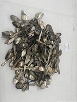 Top-down view of a large pile of assorted tarnished spoons and forks, showing a variety of handle patterns and visible tarnishing.