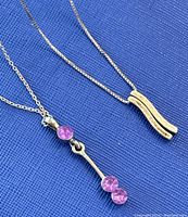 Two 925 silver necklaces on blue fabric background. One has a pendant with three pink stones, the other has a curved abstract silver pendant.