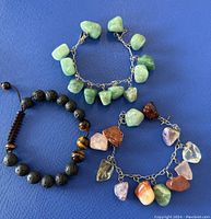 All three bracelets laid on blue background. Showing variety of stones and beads, chains and closure types.