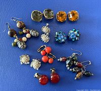 Top view of all nine pairs of vintage earrings laid on blue surface showing various styles, colors, and materials.