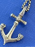 Close-up of the silver anchor pendant featuring skull and floral details on a blue background.