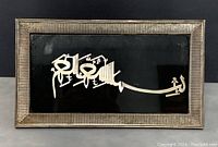 Front view showing the silver framed Islamic calligraphy on black background with textured silver frame.