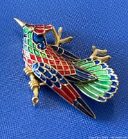 Front view showing multicolor enamel bird design on gold-tone metal