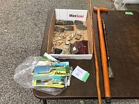 Overview photo showing box of various mens vintage items and two wooden walking sticks along with pile of postcards.