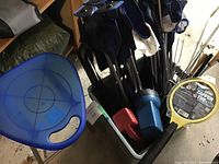 Blue plastic folding stool, assorted flashlights, bug zapper, marshmallow sticks, and various campfire tools placed together