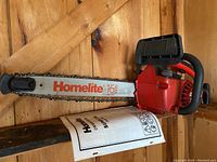 Side view of red Homelite Super 2 SL chainsaw with 16 inch bar and owner's manual underneath.