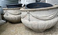 Two round concrete planters side by side with draped decorative patterns.