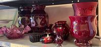 Full view of shelf with large and small cranberry glass vases, candle holder, bowl, and trinket box