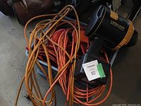 Photo showing four orange outdoor extension cords coiled on a surface next to a black and yellow battery operated work light.